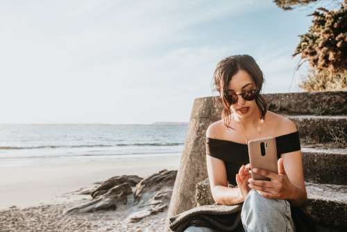 Person Sits On Steps By A Beach Looking At Their Phone Photo