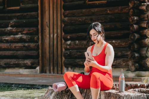 Woman Sits By A Wood Cabin And Looks At Her Phone Photo