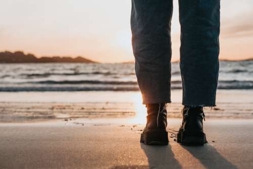 Black Boots And Legs On A Sandy Beach At Sunset Photo