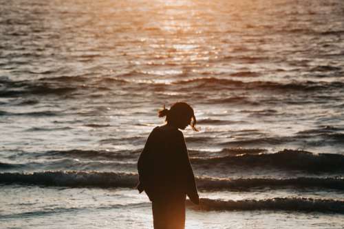 Person With Long Hair Silhouetted At Sunset By The Water Photo