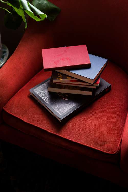 Stack Of Hardcover Books On A Red Armchair Photo