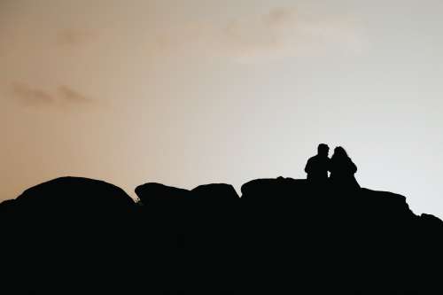 Silhouetted People Sitting On Rocks By The Setting Sun Photo