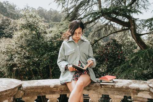 Woman Sits On A Stone Surface And Reads A Hardcover Book Photo