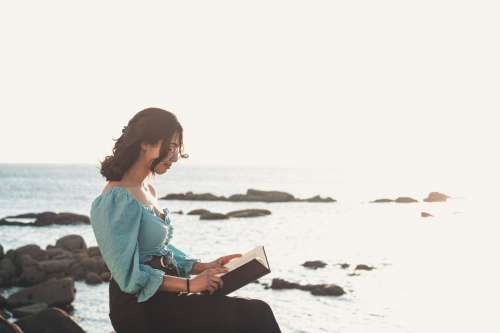 Woman Sits And Reads A Book By The Rocky Shore Photo