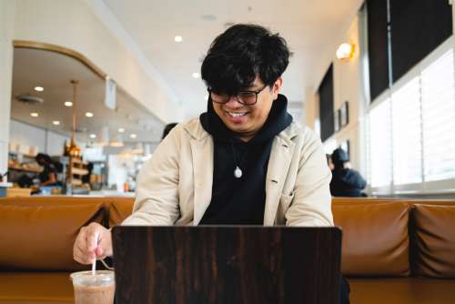 Man In Coffee Shop Sits In Front On Their Laptop On A Brown Couch Photo