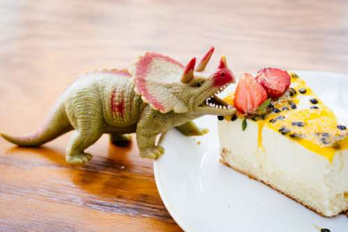 Rubber toy dinosaur about to eat a strawberry on a cake