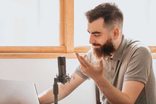 Man Sits In Front Of A Black Microphone And His Laptop Photo