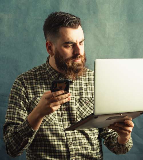 Man In Plaid Holds A Laptop And Cellphone Photo