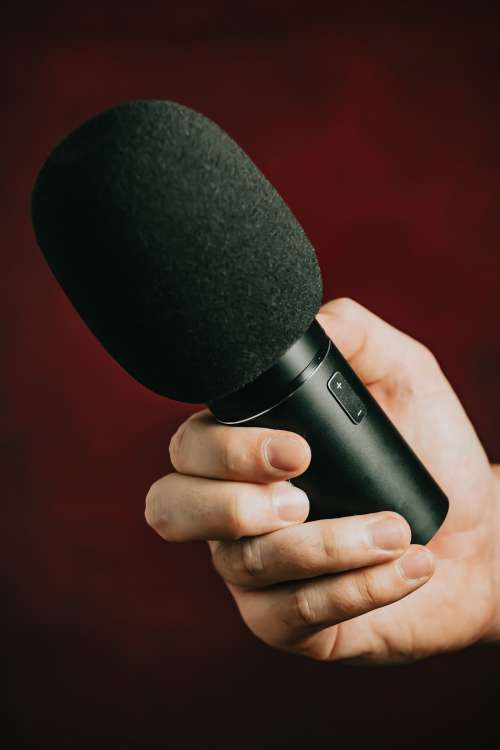 Hand Grips A Black Microphone Against Red Background Photo