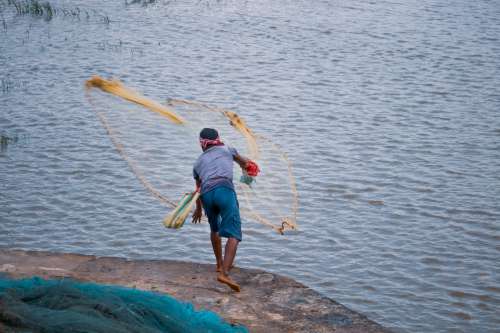 Person Throws Fishing Net Into Blue Water From The Shore Photo