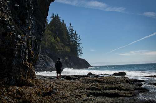 Person Stands Facing The Wild Waves On A Rocky Shore Photo