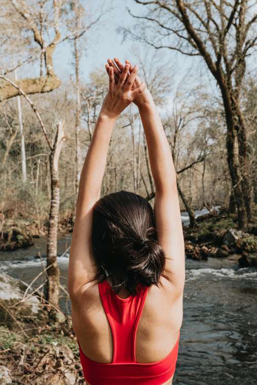 Woman In Vibrant Red Reaches Arms Up In A Stretch Outdoors Photo