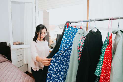 A Woman Holding A Dress Browses Her Bedroom Clothing Rack Photo
