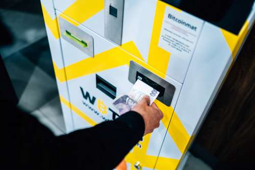 Person Places Cash Into A Yellow And White Machine Photo