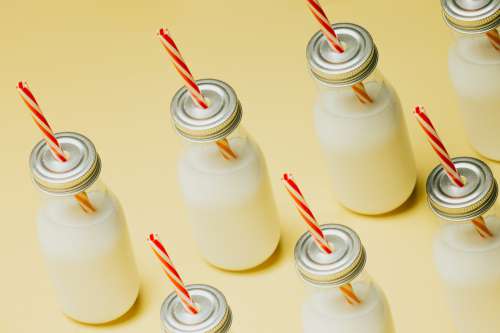 Milk Bottles With Red Striped Straws On A Yellow Surface Photo