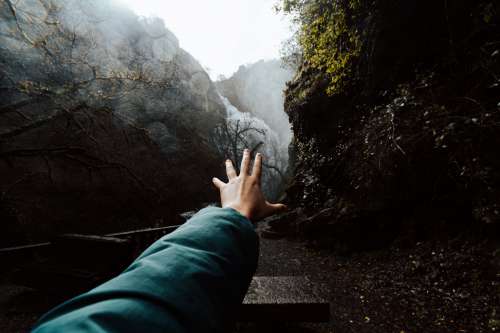 Hand Reaches Toward A Waterfall From Between Two Hills Photo