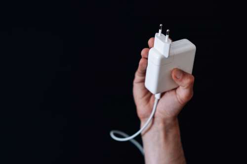 Hand Holds Up A White Square Computer Charger Photo