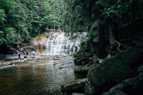 People Enjoy The Cool Water From A Forest Lined Waterfall Photo
