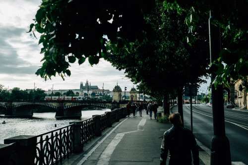People Walking On A Tree Lined Sidewalk By A River Photo