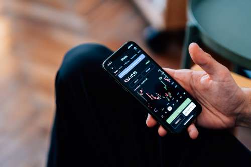 Persons Hand Holding A Phone Showing A Bitcoin Chart Photo