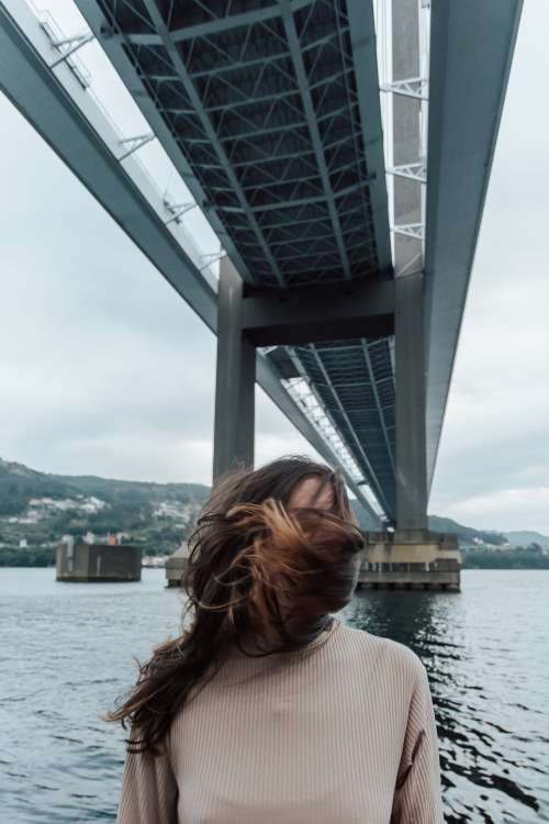 Person Covered By Hair Stands Under Bridge On A Windy Day Photo