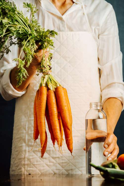 Person Holds A Glass Bottle And Carrots By Their Tops Photo