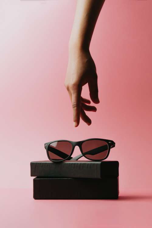 A Hand Reaches For Black Sunglasses Sitting On A Case Photo