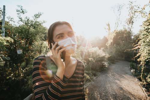 Woman In A Facemask Talks On The Phone Outdoors Photo