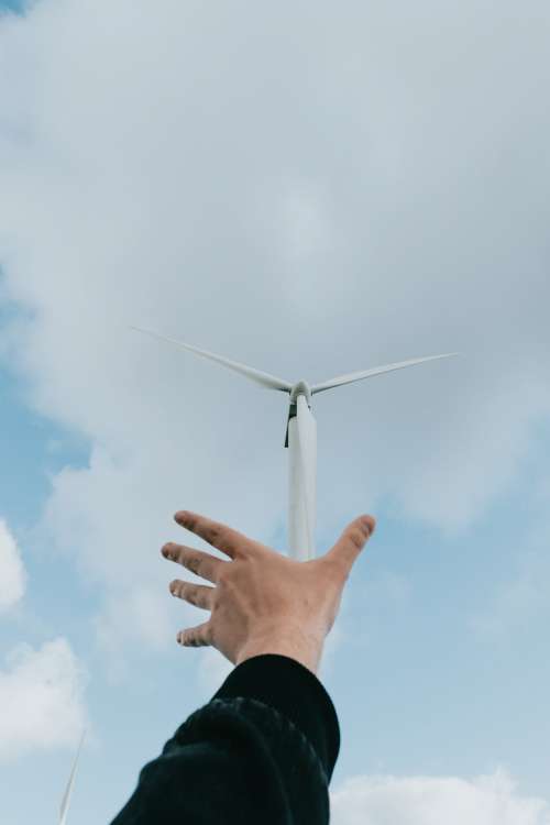 Hand Reaches Towards A Windmill On A Clear Day Photo