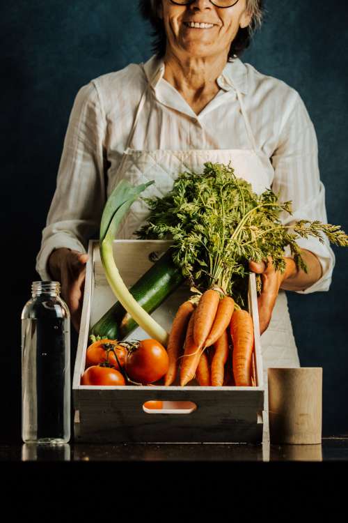 Woman Tilts A Box Of Vegetables Towards The Camera Photo