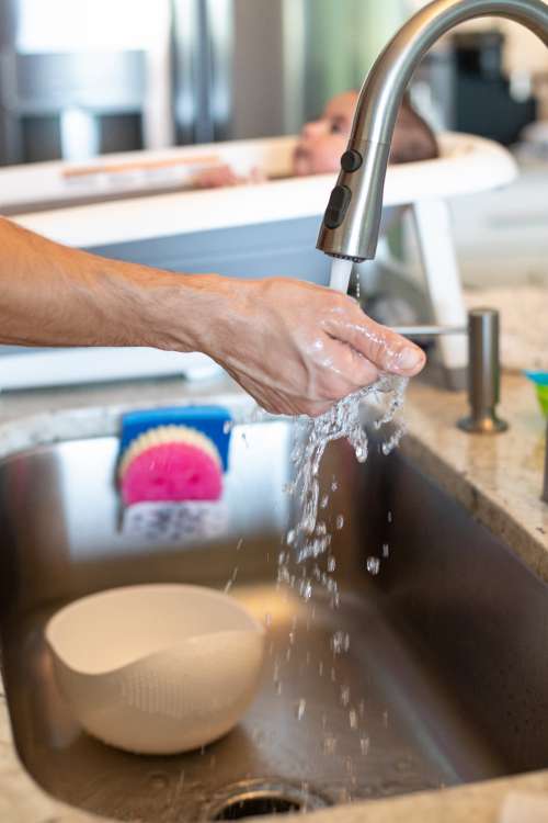 Person Holds Hand Under Running Water In Kitchen Photo