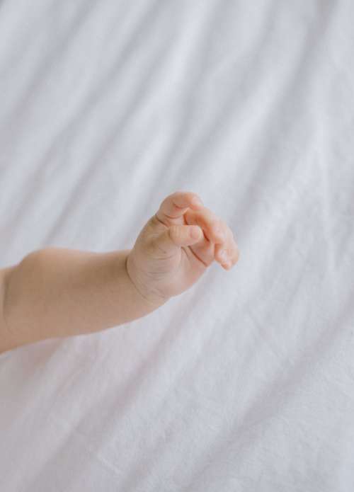 Hand Of Newborn Baby Against White Fabric Photo