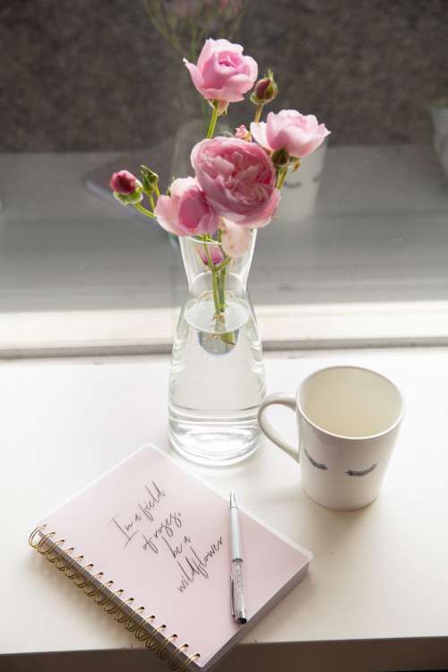Glass Vase With Pink Flowers With Notebook And A Mug Photo