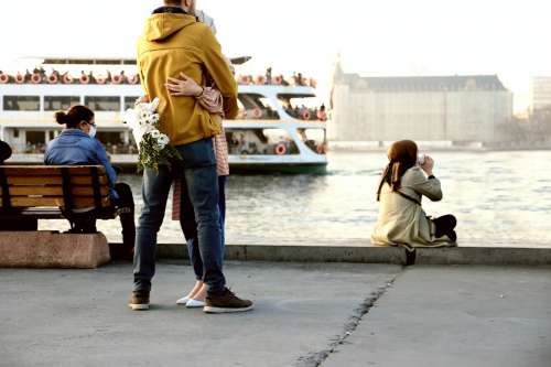 Masked People On The Boardwalk Next To Open Water Photo