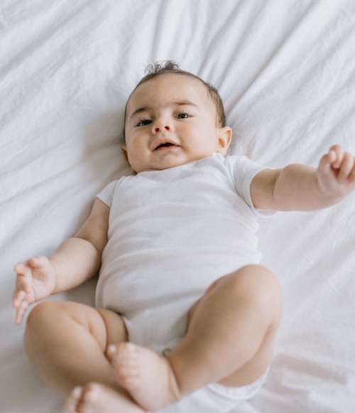 Looking Down At A Baby On Laying White Sheets Photo