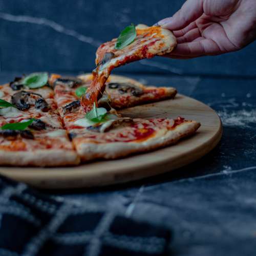 Persons Hand Lifts A Slice Of Pizza From Round Plate Photo