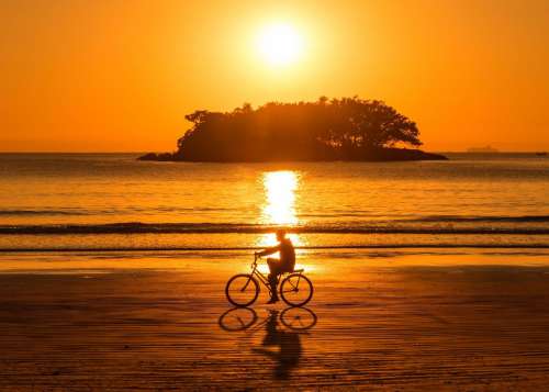 Person Riding Their Bike At Sunset Along The Beach Photo