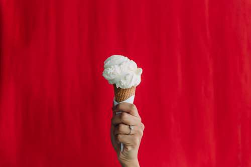Hand Holds Up A Ice Cream Cone Against Red Backdrop Photo