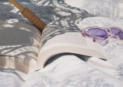 Book Lays Open Next To Purple Cateye Sunglasses Photo