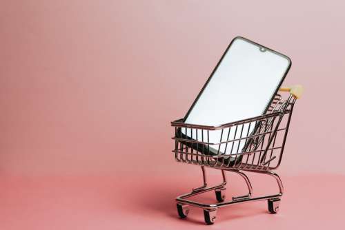 Cell Phone Sits In A Small Shopping Cart Against Pink Photo