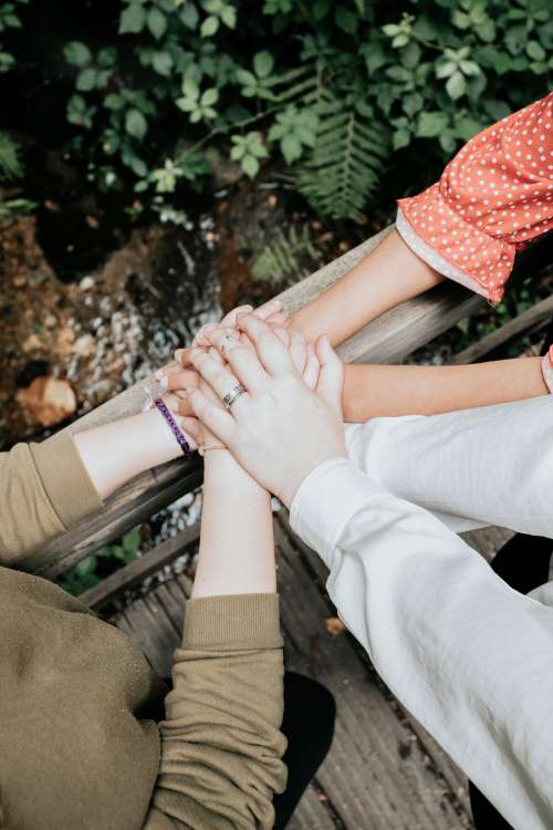 Three People Pile Their Hands Up On A Wooden Railing Photo
