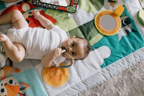 Camera Looks Down To A Baby Laying In A Colorful Mat Photo