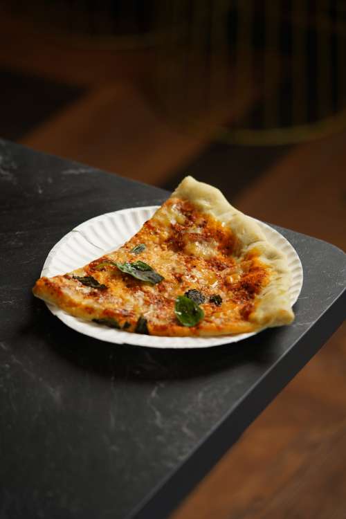 Slice Of Pizza With Fresh Basil On A White Paper Plate Photo