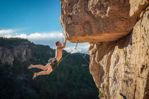 Harnessed Person Holds Onto The Edge Of A Rock Cliff Photo