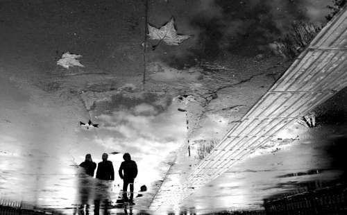 Three People Reflected In A Puddle In Black And White Photo