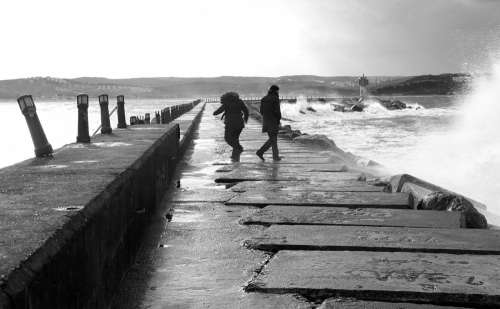 Two People Walking By Choppy Ocean Tide In Monochrome Photo