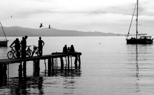 People On A Dock And Nearby Boat In Black And White Photo