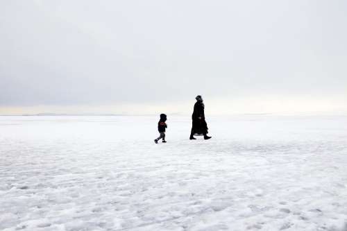 Two People In Winter Coats Walking On A Field Of Snow Photo