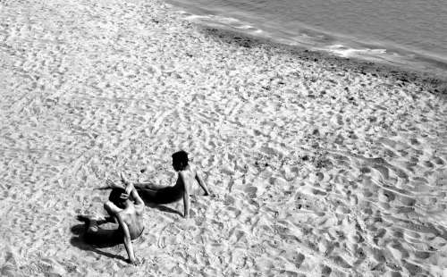 Two People Laying Back On A Sandy Beach In Black And White Photo