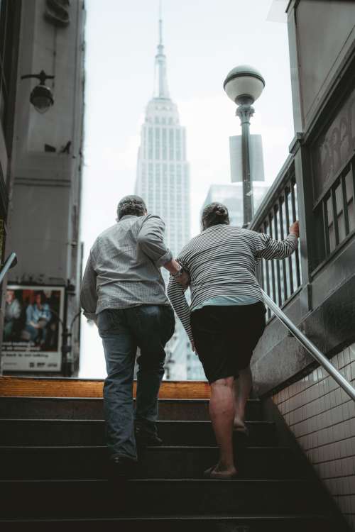 Two Help Each Other Up Subway Steps Towards A City Photo